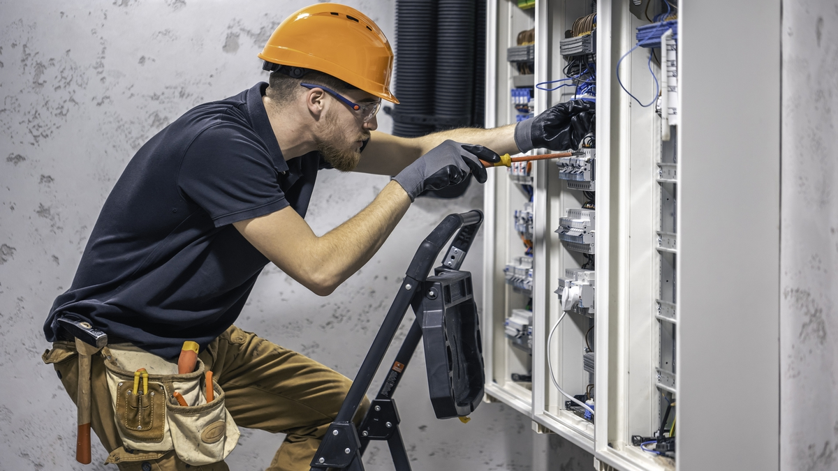 A male electrician works in a switchboard with an electrical connecting cable.