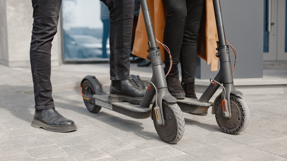 European girl anindian guy ride scooters and smile. Eco transport rental.